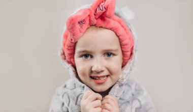 Bej arka planda izole edilmiş boyun eğik ve bornoz giyen güzel küçük bir kızın portresi.