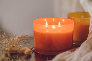 Cam kavanozdaki doğal kokulu mum ve ayna yüzeyinde yansıması olan kurumuş çiçekler..