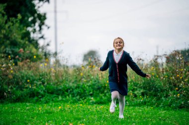 Okul üniformalı bir kız parkta koşuyor. Okul yılının başlangıcı konsepti. Okula geri dön.