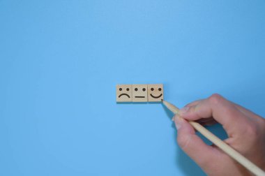 Üst kattaki müşteri elinde kalem, tahta küpte gülen yüzü mavi arka plana tercih ediyor. Hizmet derecelendirme, memnuniyet kavramı, müşteri hizmetleri değerlendirmesi ve memnuniyet anketi kavramları.