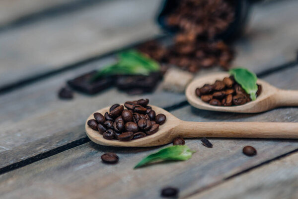 Wooden spoons with different varieties of coffee beans, dark chocolate and brown sugar on dark vintage rustic wooden background. Side view.