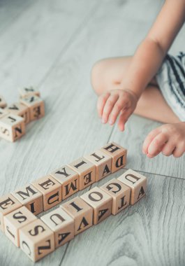 Abc küpleriyle içeride oynayan ve eğiten küçük bir kız. Küçük kız yerde tahta bloklarla oynuyor.