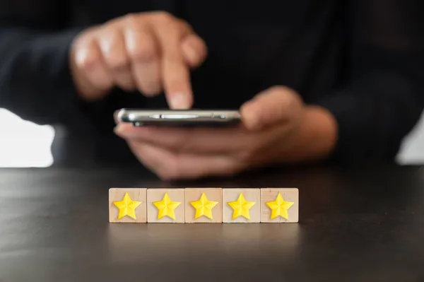 Five star rating with person holding a smartphone. Satisfaction survey concept. Customer services, best excellent business rating experience. Hand putting wooden cube with five star shape. 5 Star