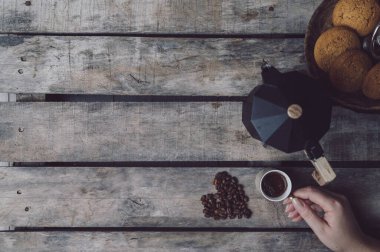 Bir kadının elleri koyu, ahşap bir masa üzerinde koyu bir kahve bardağı tutuyor.