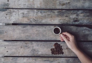 Bir kadının elleri koyu, ahşap bir masa üzerinde koyu bir kahve bardağı tutuyor.