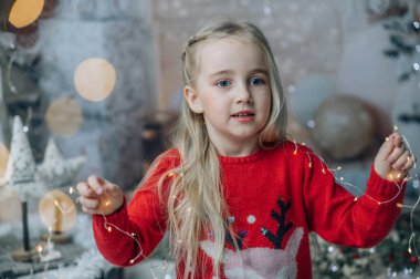 Oturma odasında yerde oturan, Noel Baba 'nın şapkasını takan ve elinde bir sürü Noel ışığı tutan güzel bir kız. Çocuk Noel süslerini hazırlıyor ve Noel Baba 'yı bekliyor.