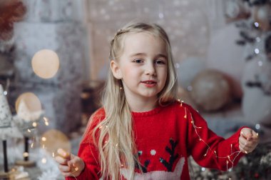 Oturma odasında yerde oturan, Noel Baba 'nın şapkasını takan ve elinde bir sürü Noel ışığı tutan güzel bir kız. Çocuk Noel süslerini hazırlıyor ve Noel Baba 'yı bekliyor.