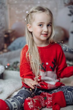 Oturma odasında yerde oturan, Noel Baba 'nın şapkasını takan ve elinde bir sürü Noel ışığı tutan güzel bir kız. Çocuk Noel süslerini hazırlıyor ve Noel Baba 'yı bekliyor.