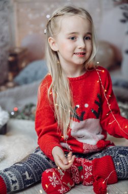 Oturma odasında yerde oturan, Noel Baba 'nın şapkasını takan ve elinde bir sürü Noel ışığı tutan güzel bir kız. Çocuk Noel süslerini hazırlıyor ve Noel Baba 'yı bekliyor.