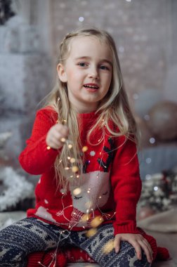 Oturma odasında yerde oturan, Noel Baba 'nın şapkasını takan ve elinde bir sürü Noel ışığı tutan güzel bir kız. Çocuk Noel süslerini hazırlıyor ve Noel Baba 'yı bekliyor.