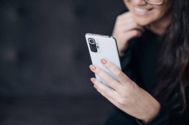 Elinde tutan, kullanan ve akıllı telefona bakan mutlu bir kadının yakın plan görüntüsü.