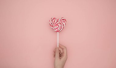 Pembe arka planda kalp şeklinde lolipop tutan kadın eli. Yaratıcı Sevgililer Günü romantik kompozisyonu düz yatar üst görünüm aşk bayramı kutlaması, kart tasarımı
