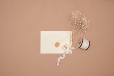 Evlilik yüzükleri, davetiyeler ve arka planda el işi zarfları. Kağıt kartların, yüzüklerin ve kurutulmuş çiçeklerin üst görüntüsü, kopyalama alanı. Hatırlanabilir tarih düzenleme kavramı