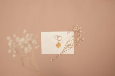 Evlilik yüzükleri, davetiyeler ve arka planda el işi zarfları. Kağıt kartların, yüzüklerin ve kurutulmuş çiçeklerin üst görüntüsü, kopyalama alanı. Hatırlanabilir tarih düzenleme kavramı