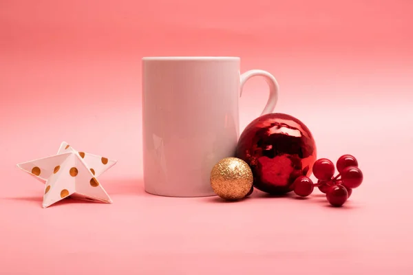 Pembe arka planda Noel süsleri olan büyük beyaz kahve kupası.