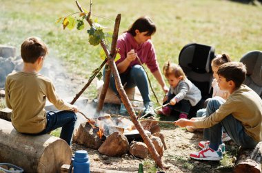 Dağda aile şenliği ateşi. Kızarmış sosis. Anne ve dört çocuğu kamp yapıyor. Sonbahar yürüyüşü ve kamp havası. Ateşin yanında ısınmak ve yemek pişirmek. 
