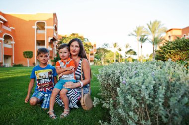 Mısır tatil köyünde yeşil çimlerde oturan iki oğlu olan bir anne. Aile tatili.