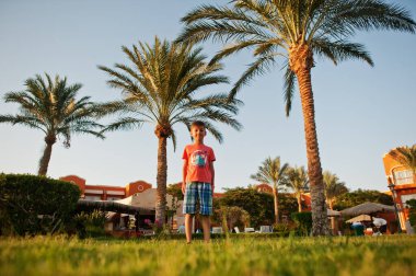 Mısır tatil köyü bahçesinde palmiyelerin yanında duran komik çocuk..