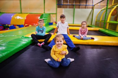 Çocuklar kapalı oyun merkezinde oynuyor ve trambolinde oturuyor. Dört çocuklu büyük bir aile..