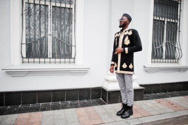 Geleneksel ceket giymiş mega stil Afrikalı bir adam. Şapkalı, güneş gözlüklü, elinde puro olan şık siyahi bir adam..