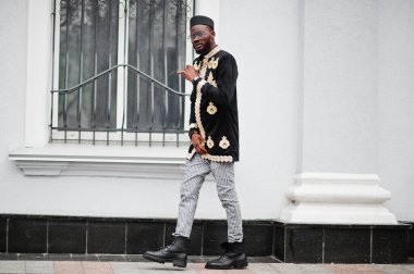 Geleneksel ceket giymiş mega stil Afrikalı bir adam. Şapkalı, güneş gözlüklü, elinde puro olan şık siyahi bir adam..
