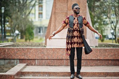 Geleneksel giysili, güneş gözlüklü ve siyah şapkalı Afrikalı şık ve yakışıklı bir adam anıtın önünde dikiliyor..