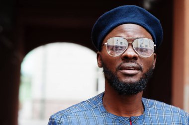 Mavi otantik kostümlü, gözlüklü ve bereli Afrikalı adam. Moda Nijeryalı Adam.