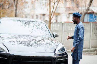 Mavi otantik kostümlü, gözlüklü ve bereli Afrikalı adam. Siyah SUV arabasının yanında şık bir Nijeryalı..