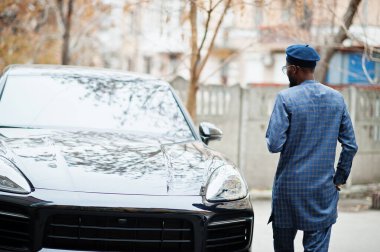 Mavi otantik kostümlü, gözlüklü ve bereli Afrikalı adam. Siyah SUV arabasının yanında şık bir Nijeryalı..