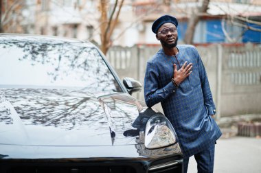 Mavi otantik kostümlü, gözlüklü ve bereli Afrikalı adam. Siyah SUV arabasının yanında şık bir Nijeryalı..