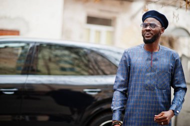 Mavi otantik kostümlü, gözlüklü ve bereli Afrikalı adam. Siyah SUV arabasının yanında şık bir Nijeryalı..