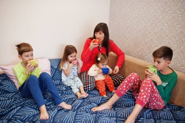 Mutlu büyük aile yatak odasında birlikte eğleniyor. Geniş aile sabahı konsepti. Dört çocuklu anne pijama giyer evde çay içer..