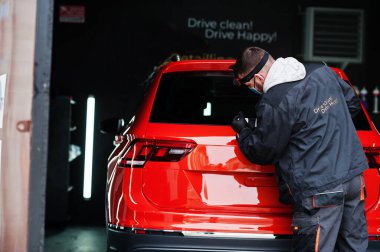 Araba temizleme konsepti. Yörünge parlatıcısı olan maskeli bir adam tamircide turuncu SUV araba cilalıyor..