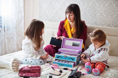 Mother and daughters doing makeup on the bed in the bedroom.