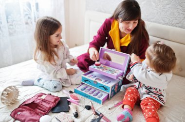 Mother and daughters doing makeup on the bed in the bedroom.