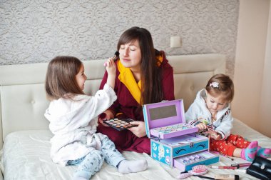Mother and daughters doing makeup on the bed in the bedroom.