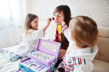 Mother and daughters doing makeup on the bed in the bedroom.