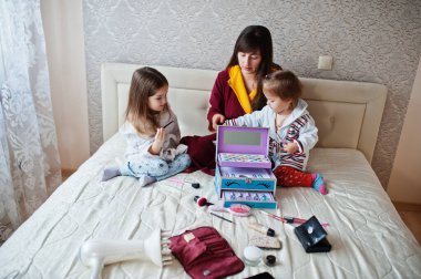 Mother and daughters doing makeup on the bed in the bedroom.