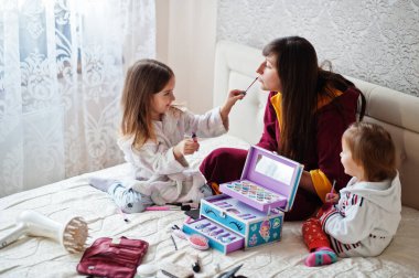 Mother and daughters doing makeup on the bed in the bedroom.