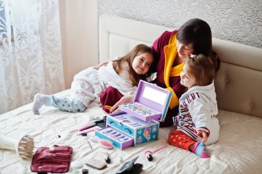 Mother and daughters doing makeup on the bed in the bedroom.