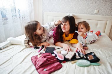 Mother and daughters doing makeup on the bed in the bedroom.