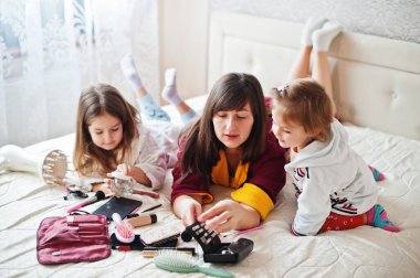 Mother and daughters doing makeup on the bed in the bedroom.