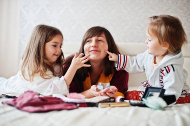 Mother and daughters doing makeup on the bed in the bedroom.