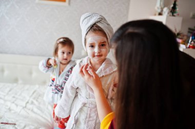 Mother with daughters in a bathrobe with a towel on her head take care of the skin at home, cucumbers on eyes.