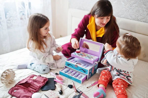 Mother and daughters doing makeup on the bed in the bedroom.