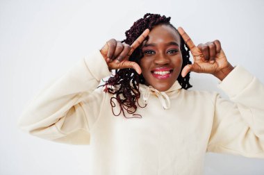African woman in hoodie stand against white wall and show frame on head by fingers.