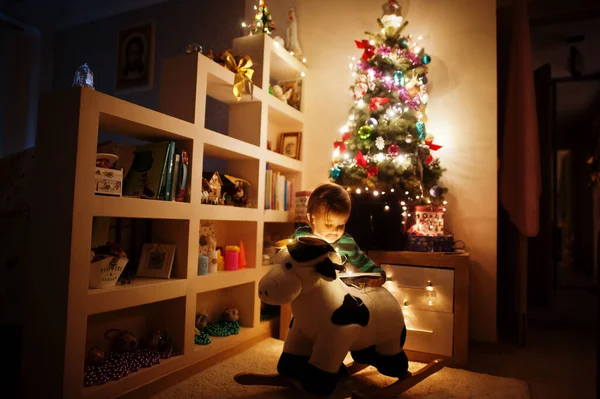 晚上回家的时候 小女孩躺在圣诞树上摇着奶牛玩具 戴着闪亮的花环 — 图库照片