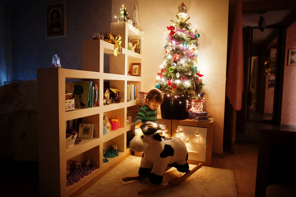 Baby Girl Rocking Cow Toy Christmas Tree Shining Garlands Evening — Zdjęcie stockowe
