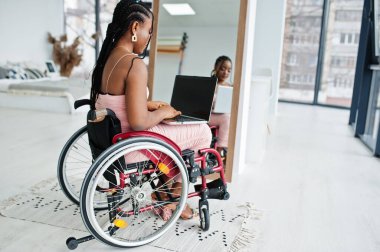 Genç, engelli, tekerlekli sandalyede oturan, aynaya karşı dizüstü bilgisayarla çalışan Afro-Amerikan kadın..