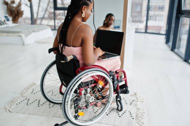 Genç, engelli, tekerlekli sandalyede oturan, aynaya karşı dizüstü bilgisayarla çalışan Afro-Amerikan kadın..